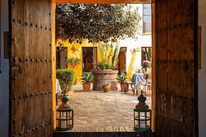 An open wooden door leading to a courtyard with potted plants, a table with a blue tablecloth, and lanterns. - Cortijo Boutique Marbella (Marbella)