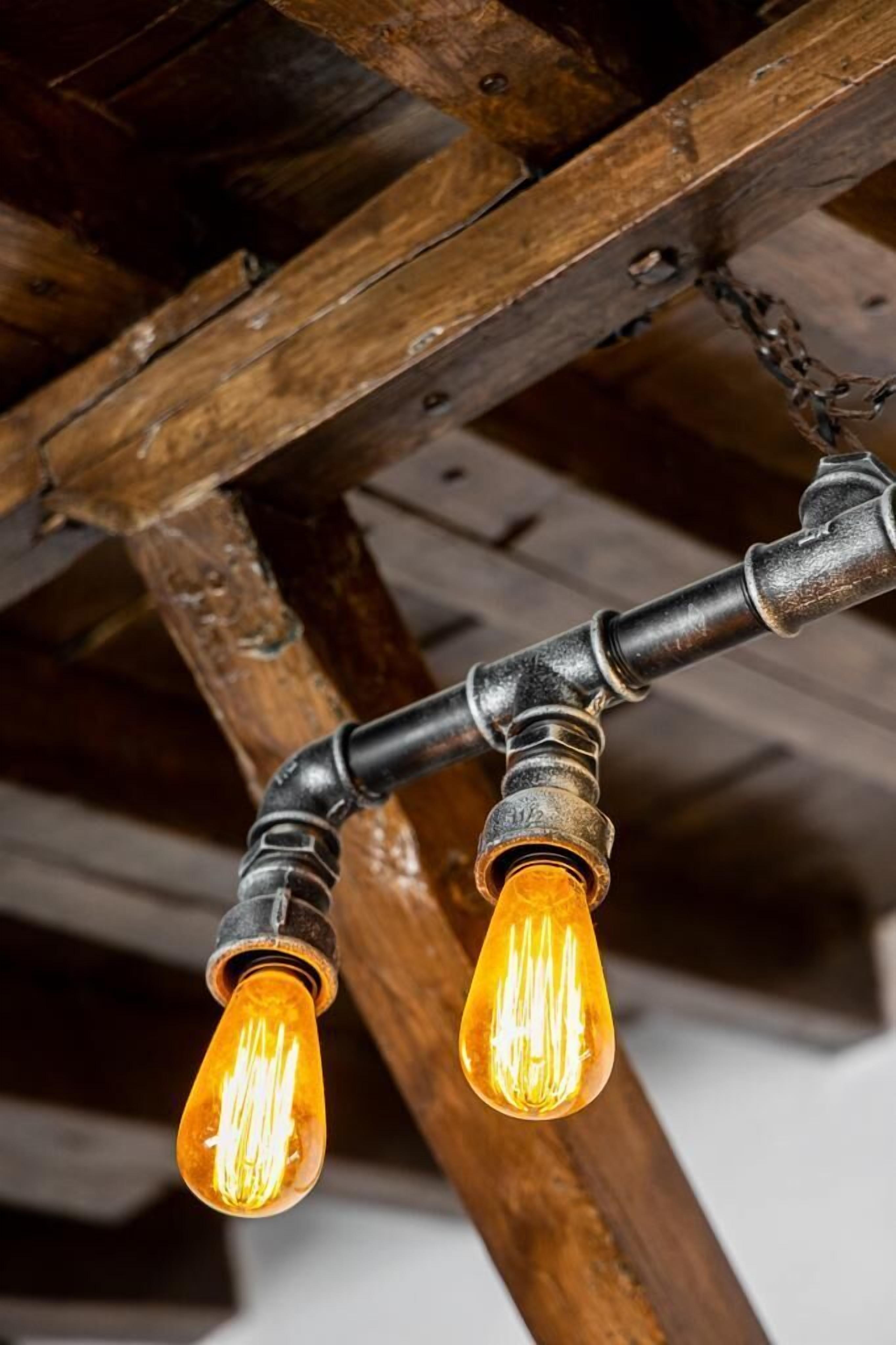 Ett rustikt tak med synliga träbjälkar och två hängande glödlampor i Edison-stil.