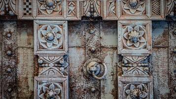 A weathered wooden door with intricate floral carvings and metal hardware.