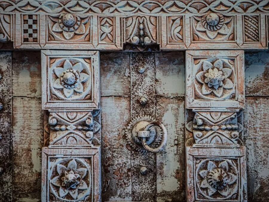 A weathered wooden door with intricate floral carvings and metal hardware.
