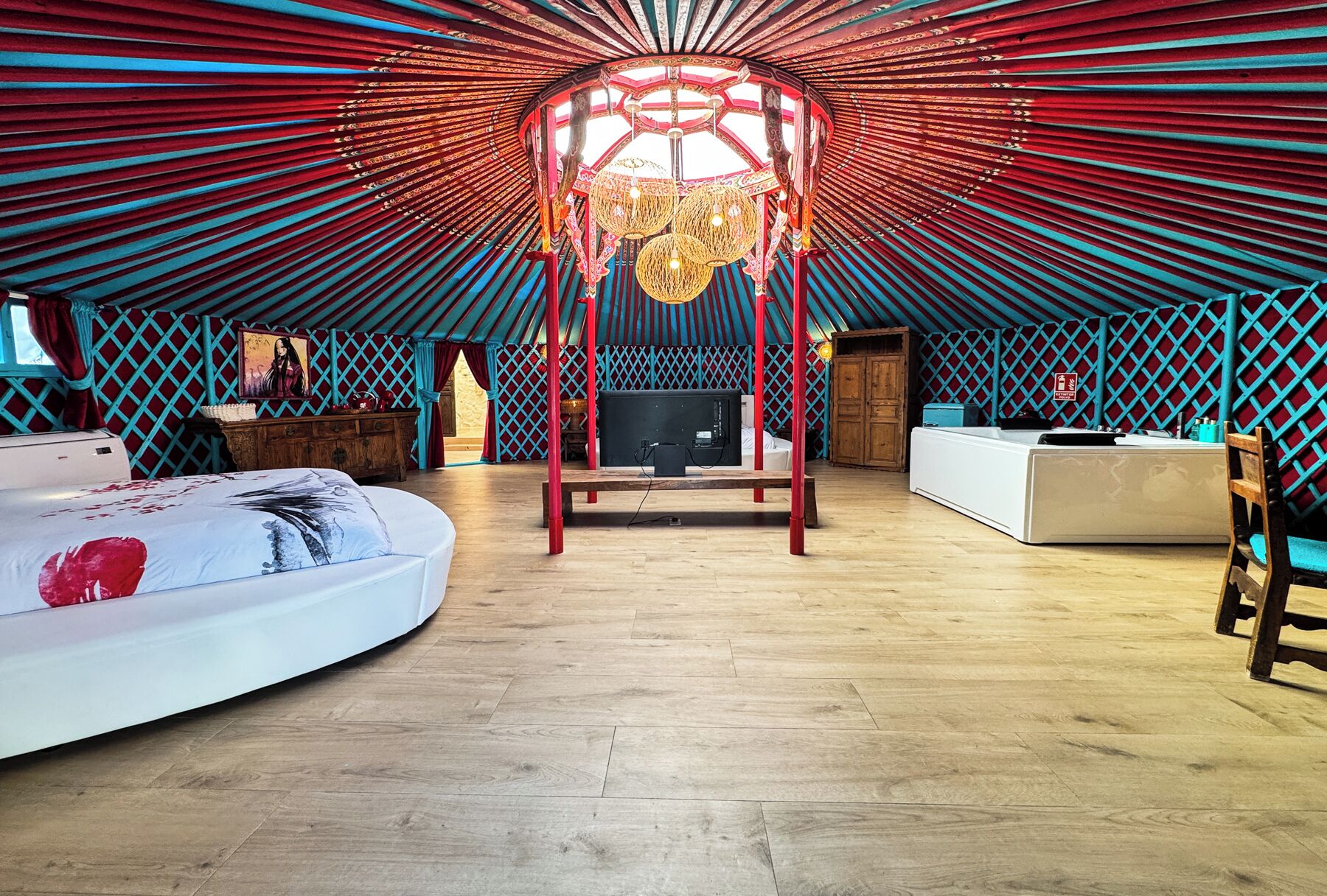 A yurt-style room with a central wooden structure, a bed, a desk, and a television.