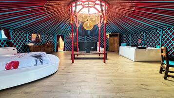 A yurt-style room with a central wooden structure, a bed, a desk, and a television.
