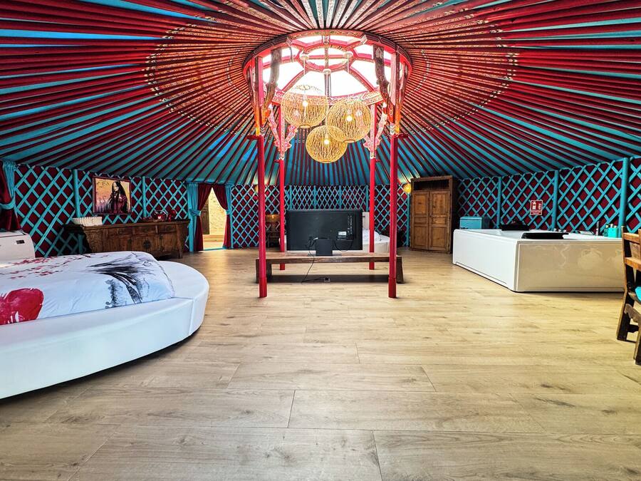A yurt-style room with a central wooden structure, a bed, a desk, and a television.
