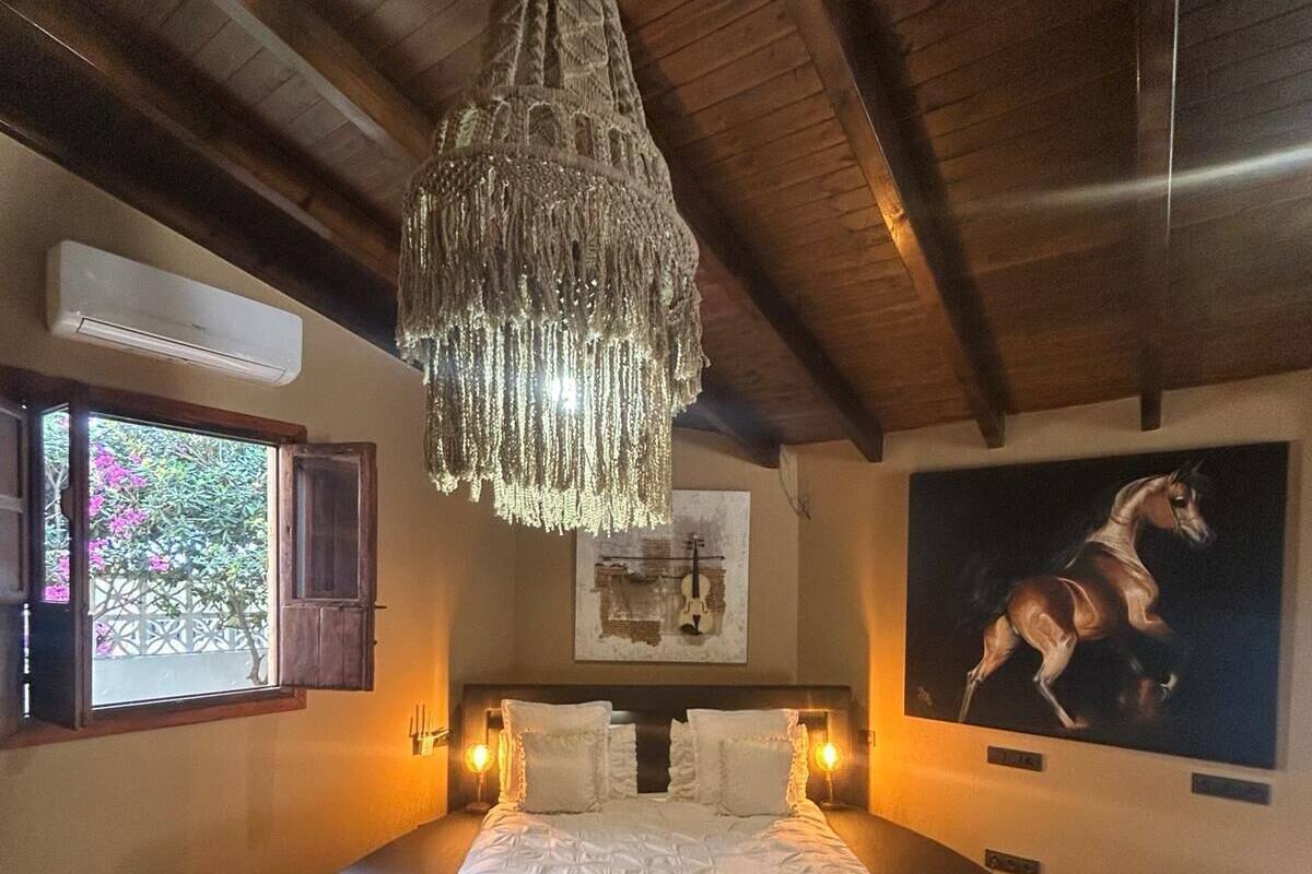 Une chambre à coucher avec un grand lit, un lustre, un tableau représentant un cheval et des poutres en bois au plafond.