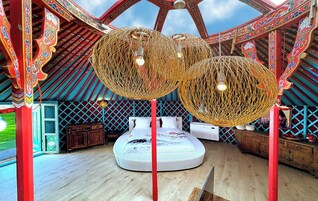 Een kamer met een rond bed, een grote geweven hanglamp en traditionele decoratie.