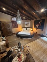 Een gezellige slaapkamer met een groot bed, houten balken, een kroonluchter en een rustieke eettafel met diverse voorwerpen.