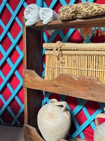 Een rustieke houten plank met een geweven mand, een witte handdoek, een kussen met luipaardprint en een terracotta pot.
