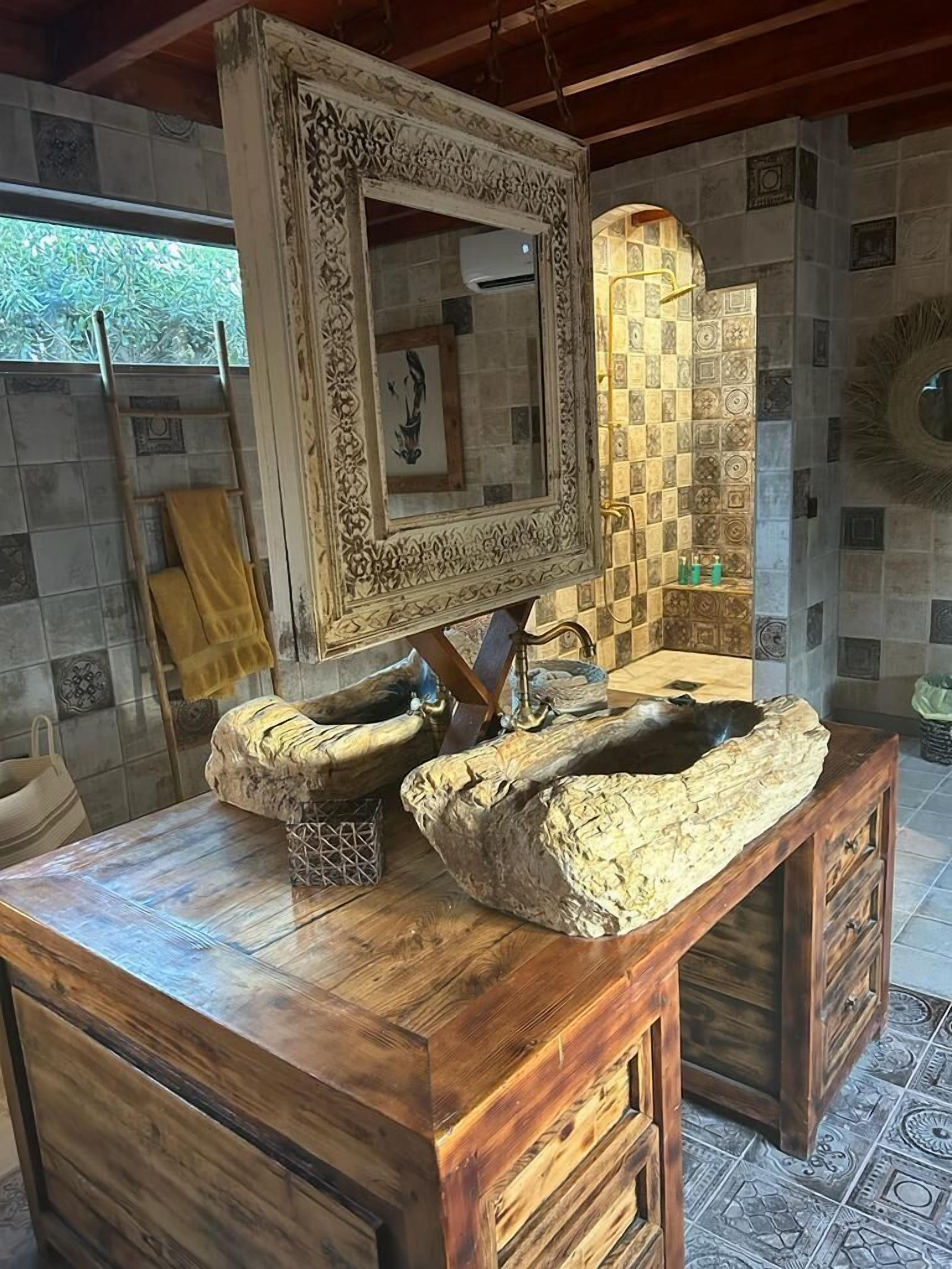A wooden vanity with a large mirror, a sink, and a decorative stone basin.