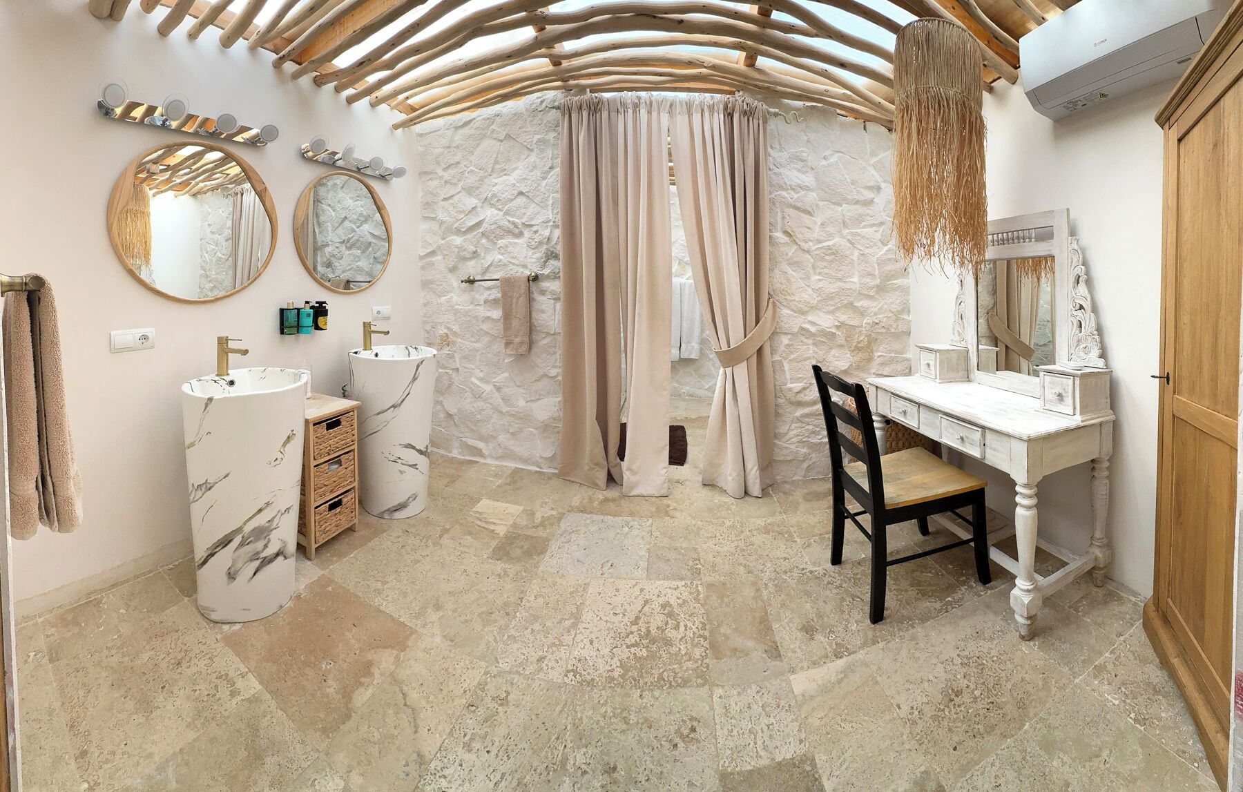 A bathroom with a stone wall, two sinks, a vanity with a mirror, and a wooden chair.