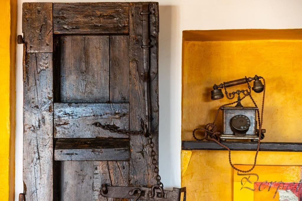 A rustic wooden door with a metal chain lock and a vintage telephone on a yellow wall.