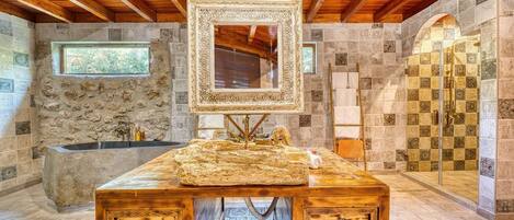 A stone-walled bathroom with a wooden vanity, a large mirror, and a shower area.
