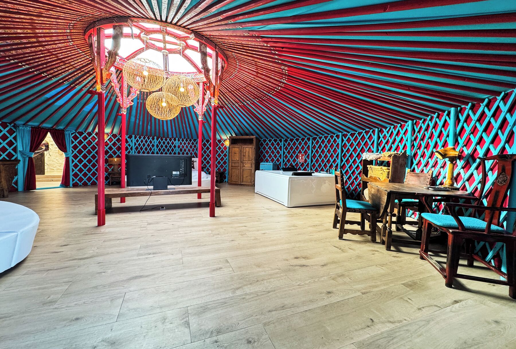 Una yurta con suelo de madera, un área central de estar con un banco y una mesa con sillas.
