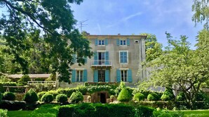 Un bâtiment à deux étages doté d’un balcon, entouré de haies et d’arbres bien entretenus.