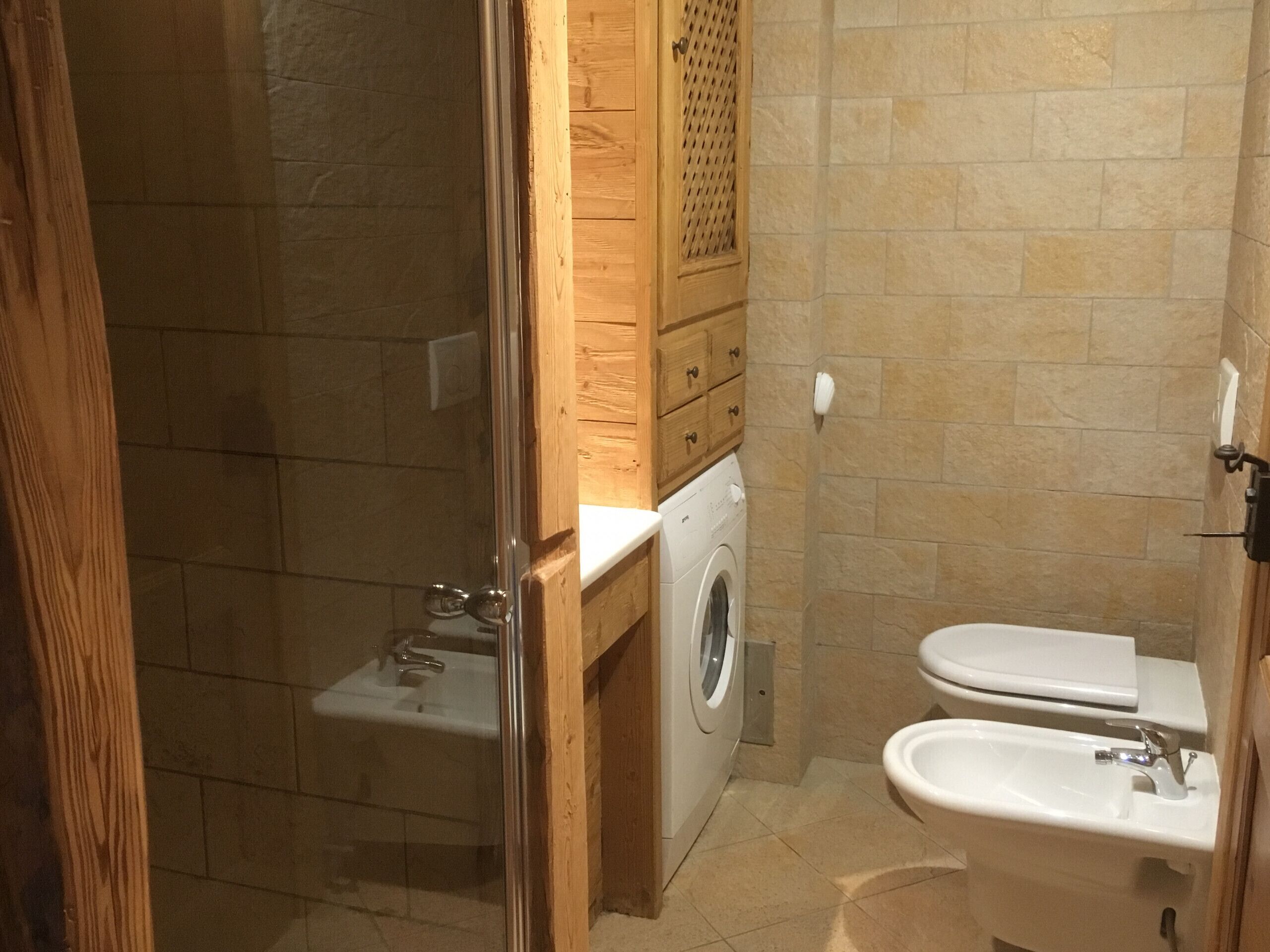 A compact bathroom with a glass shower enclosure, a washing machine, and two sinks.