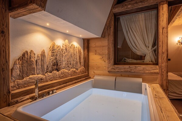 A bathroom with a large bathtub, wooden wall paneling, and a decorative rock wall.