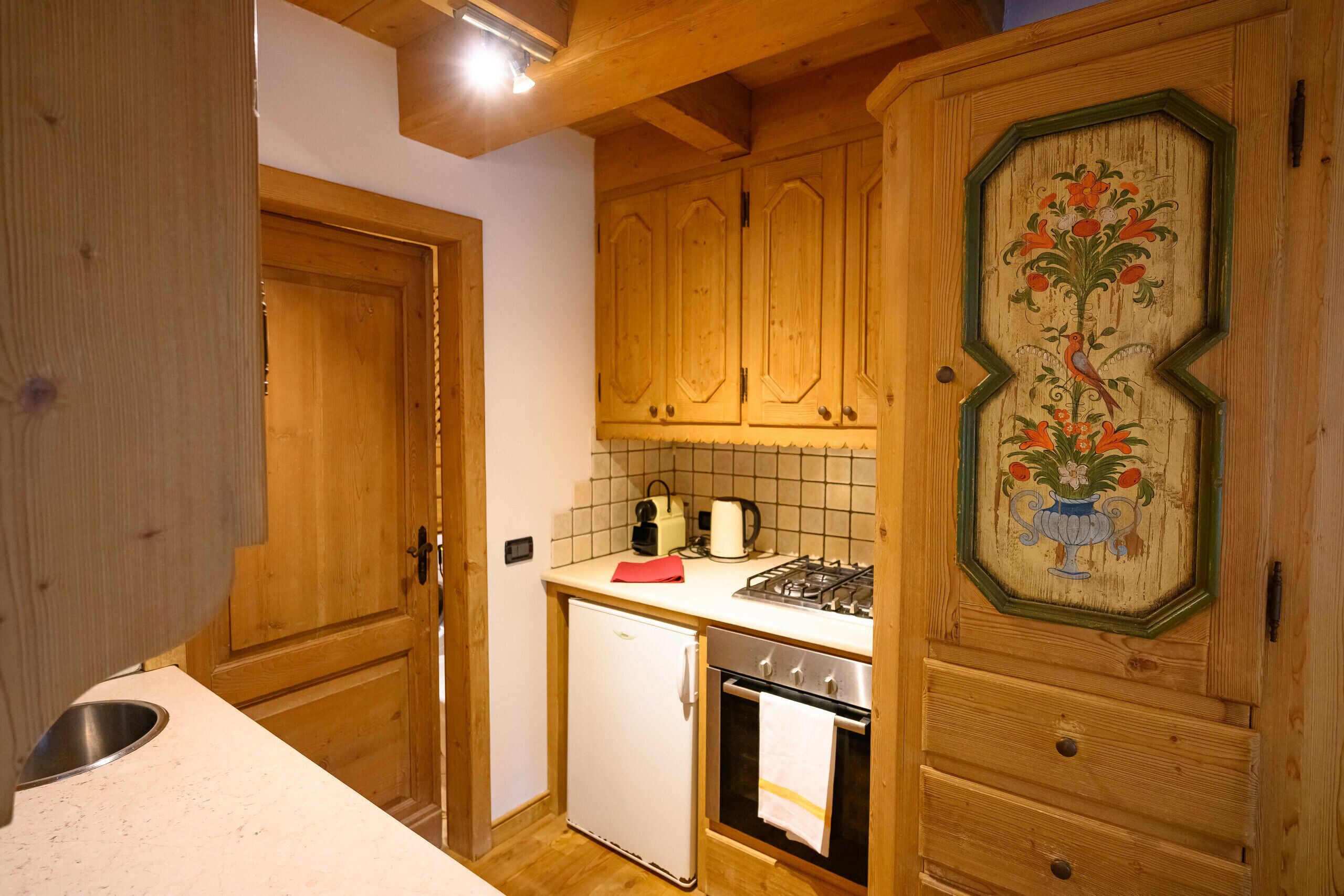 Een kleine keuken met houten kastjes, een kleine koelkast, een fornuis en een betegelde spatwand.