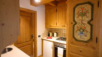 Een kleine keuken met houten kastjes, een kleine koelkast, een fornuis en een betegelde spatwand.