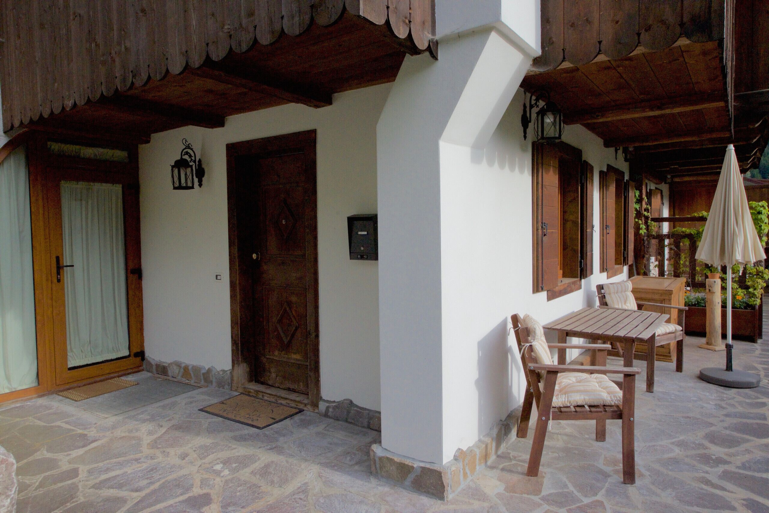 Eine Terrasse mit Steinboden, Holzmöbeln und einer Tür.