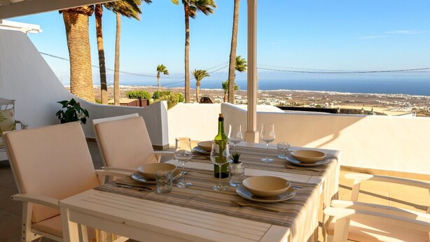 An outdoor dining area with a table set for four, overlooking a coastal landscape with palm trees and a view of the sea. - Villa Palma Lanzarote (Tías)