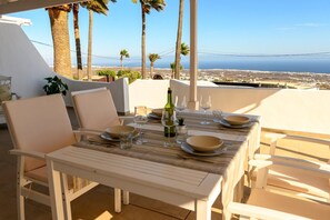 An outdoor dining area with a table set for four, overlooking a coastal landscape with palm trees and a view of the sea. - Villa Palma Lanzarote (Tías)