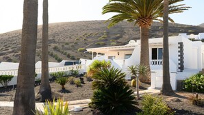 A white building with a flat roof, surrounded by palm trees and desert vegetation. - Villa Palma Lanzarote (Tías)