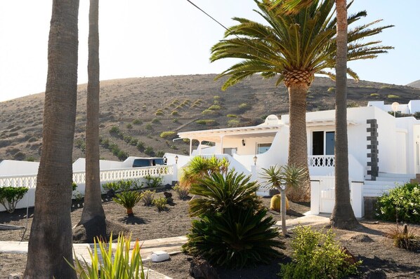 A white building with a flat roof, surrounded by palm trees and desert vegetation. - Villa Palma Lanzarote (Tías)