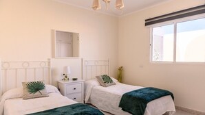 A bedroom with two beds, a bedside table with a lamp, a mirror, and a window. - Villa Palma Lanzarote (Tías)