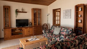 A living room with a wooden TV stand, a floral sofa, a coffee table, and a bookshelf. - Villa Palma Lanzarote (Tías)