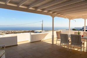 A covered terrace with a view of the sea, white chairs, and a table with a bottle and glass. - Villa Palma Lanzarote (Tías)