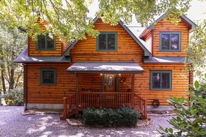 A log cabin with a front porch, multiple windows, and a chimney.