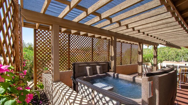 Un jacuzzi bajo una pérgola con fondo de celosía, rodeado de follaje.