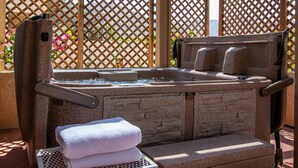 Tinaja de piedra con escalones, una toalla y una silla de metal en un espacio al aire libre sombreado, con un fondo de celosía de madera.