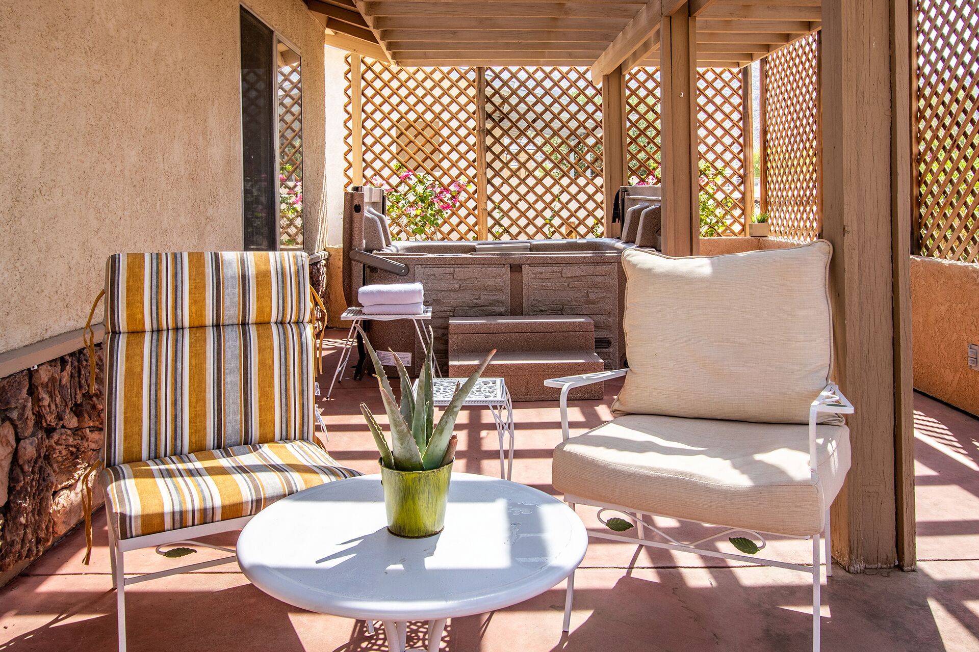 An outdoor patio with a stone bench, striped sofa, and a round table with a plant.