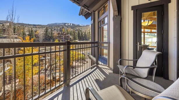 A balcony with a view of a mountainous landscape, a chair, and a door with a light fixture.