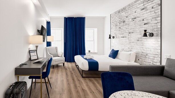 Ein modernes Hotelzimmer mit einem Bett, einem Schreibtisch, einem Sessel, einer Couch und einer Wand mit Ziegelsteinverkleidung.