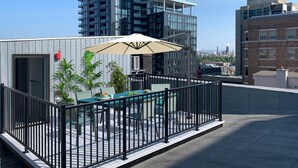 Eine Dachterrasse mit Tisch und Stühlen, umgeben von einem schwarzen Metallgeländer.