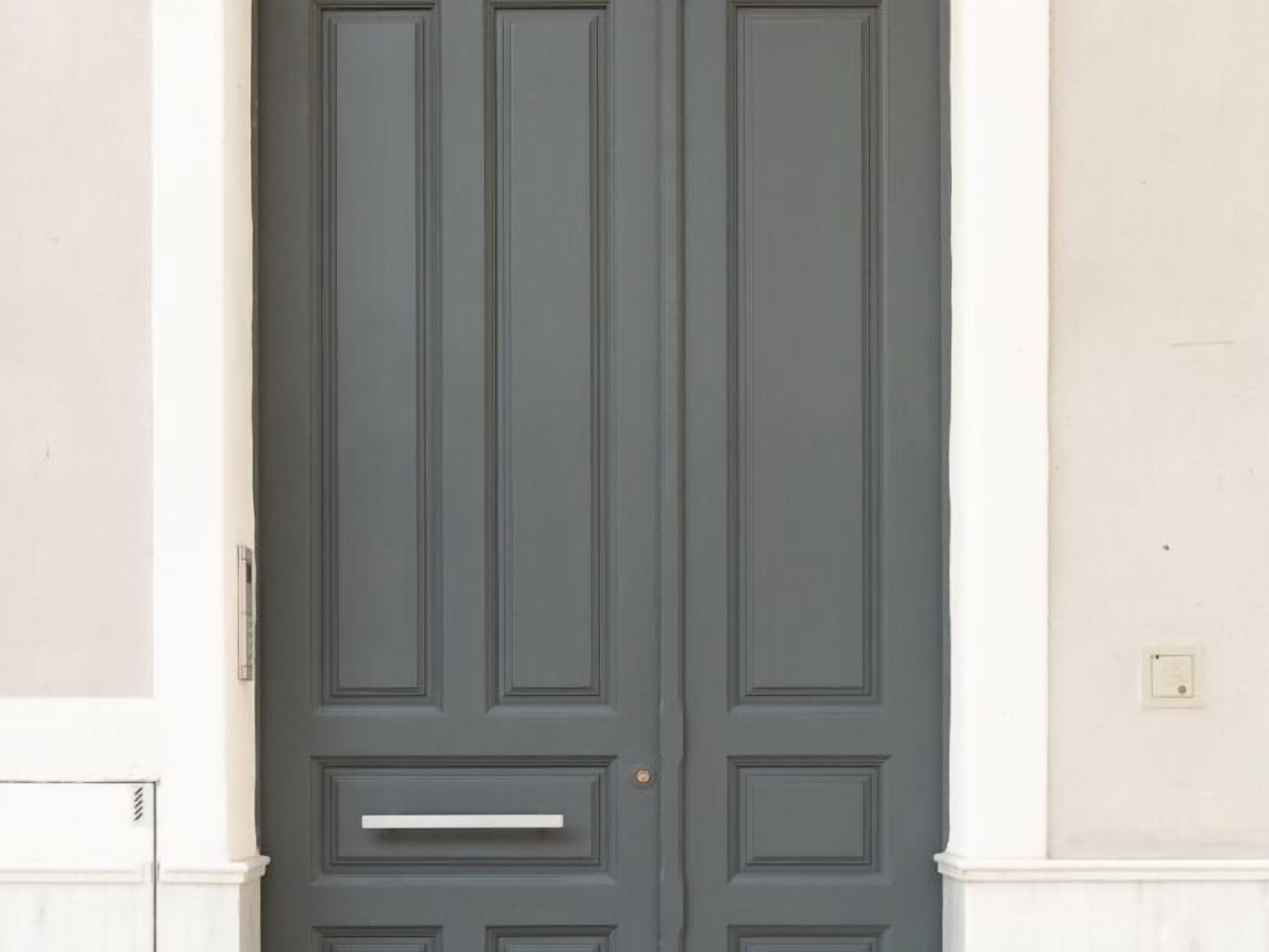 A closed dark grey door with a handle and a small rectangular shelf below it, set in a building with white trim and a light-colored wall.
