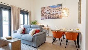 Un salon moderne avec un canapé gris, des fauteuils orange et une table à manger dressée pour quatre personnes.