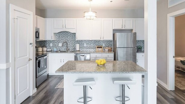 A modern kitchen with white cabinets, a granite countertop, and a central island with bar stools.