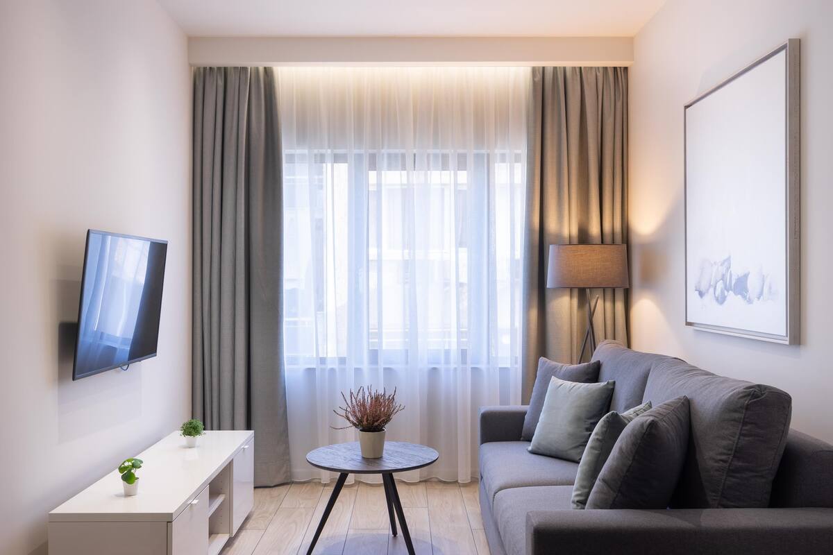 Una sala de estar moderna con un sofá, una mesita con una planta, un televisor y una lámpara.