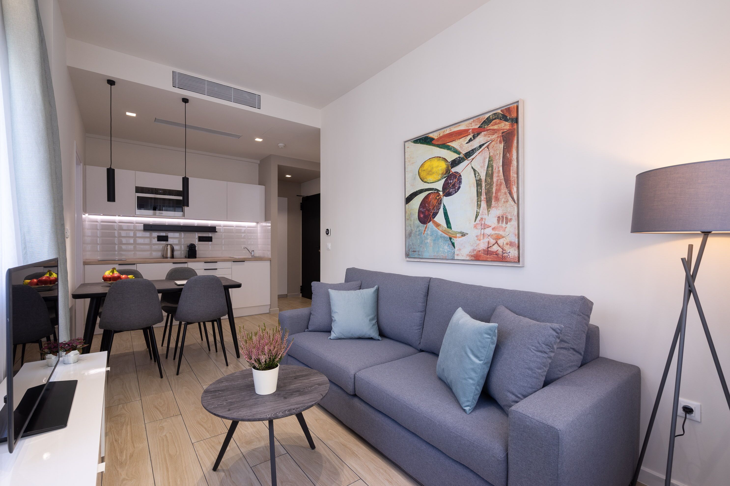 Ein modernes Wohnzimmer mit einem grauen Sofa, einem Esstisch mit Stühlen und einer Küche im Hintergrund.