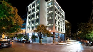 A modern multi-story building with a prominent corner entrance, large windows, and a visible tree in front. - Hestia - Ippokratous 35 (Athens)
