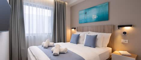 A modern hotel room with a large bed, a bedside table with a lamp, a painting on the wall, and a window with curtains.