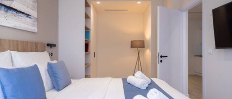A hotel room with a bed, pillows, a blue towel, a lamp, and a TV.