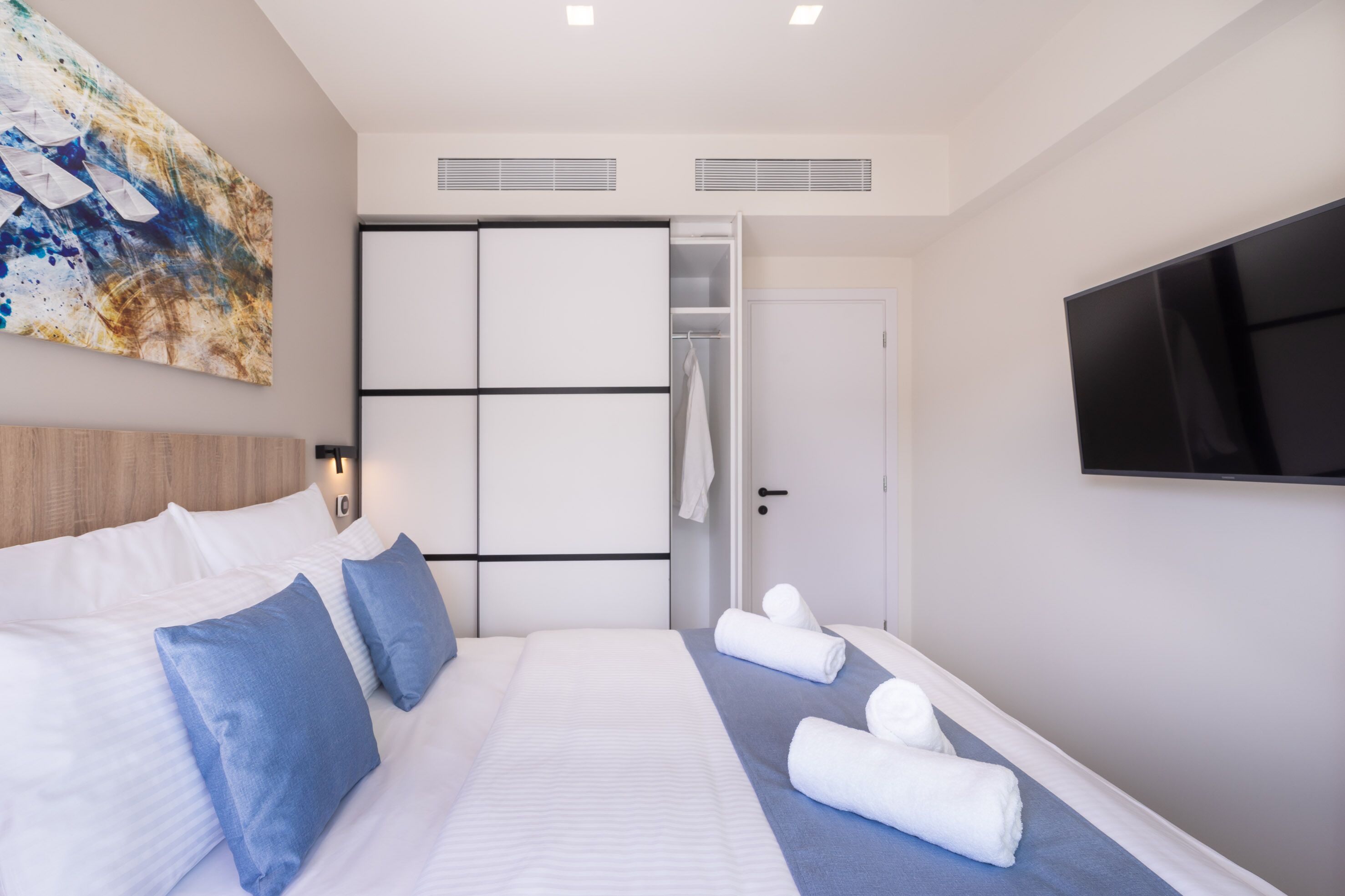 A modern hotel room with a large bed, a walk-in closet, a flat-screen TV, and a large abstract painting on the wall.