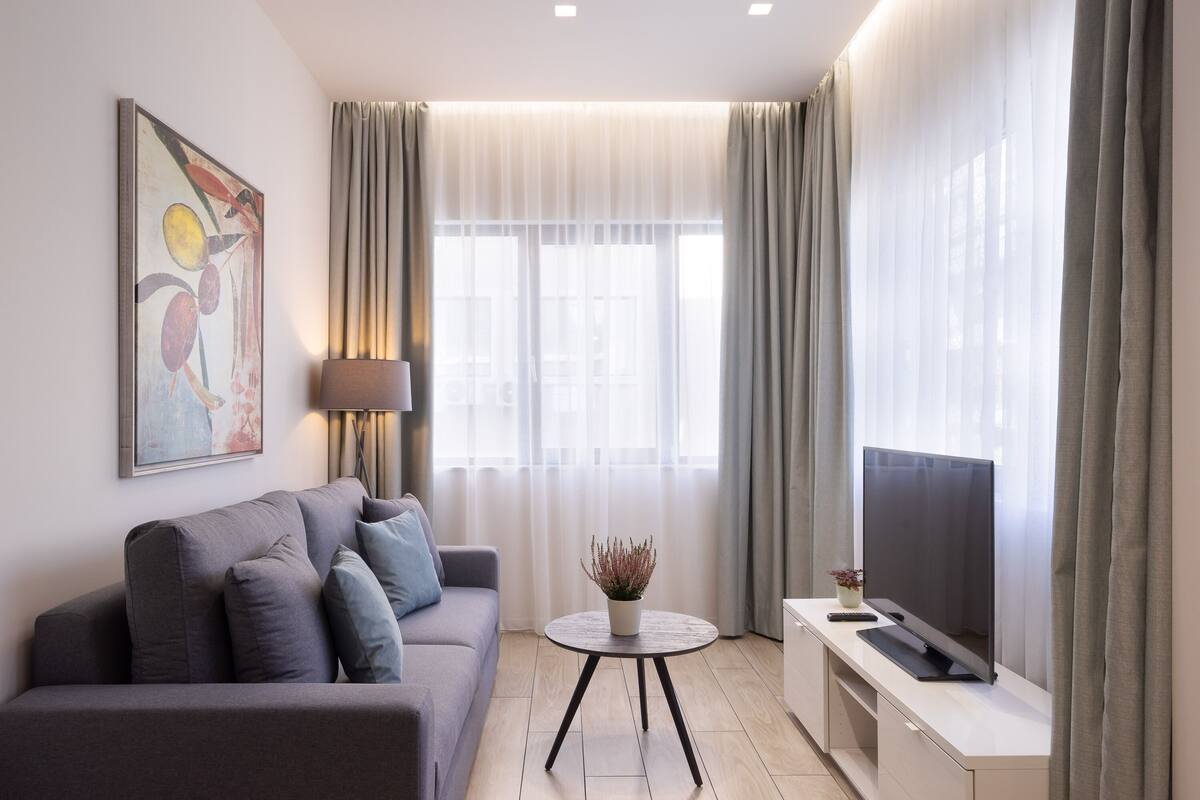 Un salón moderno con un sofá gris, una mesa redonda de centro, un televisor de pantalla plana y un cuadro en la pared.