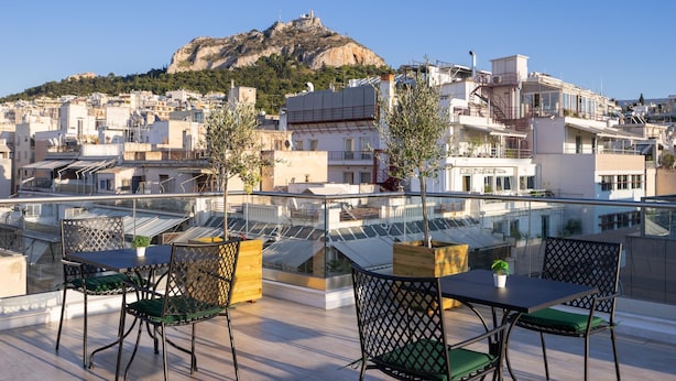 A rooftop terrace with a table and chairs, overlooking a cityscape with buildings and a hill. - Hestia - Ippokratous 35 (Athens)