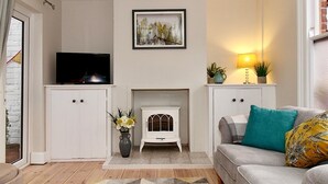 A living room with a fireplace, a sofa, a TV, and a patterned rug. - A Character Cottage in Historical Canterbury - Pass the Keys (Canterbury)