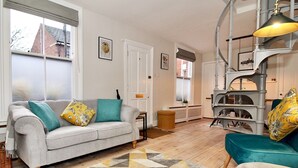 A living room with a grey sofa, teal cushions, a geometric rug, and a staircase with a vintage-style lamp. - A Character Cottage in Historical Canterbury - Pass the Keys (Canterbury)