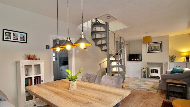 A spacious living room with a wooden dining table, grey sofas, and a spiral staircase. - A Character Cottage in Historical Canterbury - Pass the Keys (Canterbury)